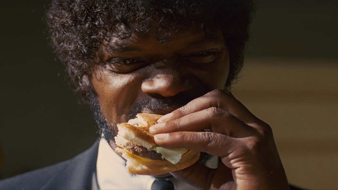 Scena z filmu "Pulp Fiction". Zbliżenie na twarz postaci. Jules Winniefield je hamburgera.