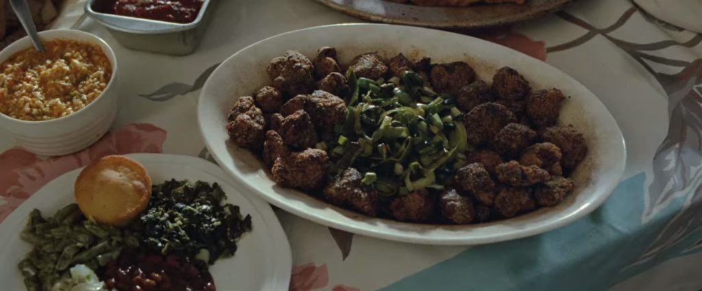 Scena z filmu "Diabeł wcielony". Usmażona w panierce wątróbka na talerzu, wokół na stole inne potrawy przyniesione jako dar.