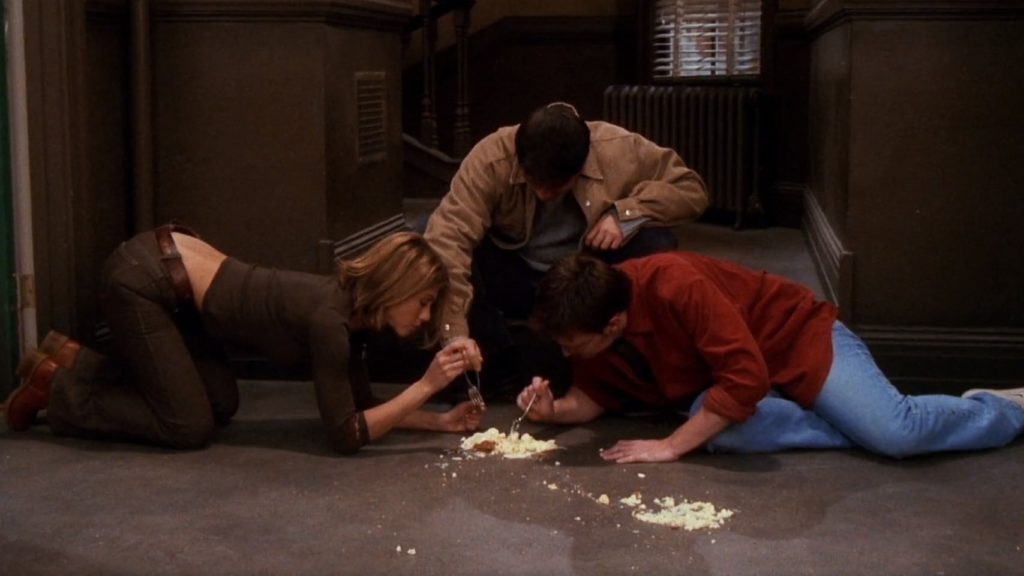 Scena z serialu "Przyjaciele". Rachel i Chandler jedzą sernik z podłogi, dołącza do nich Joey.