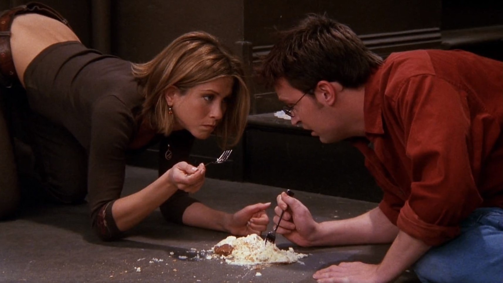 Scena z serialu "Przyjaciele". Rachel i Chandler jedzą sernik z podłogi.