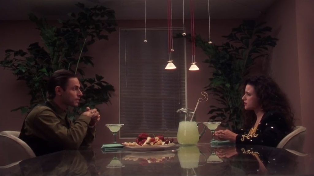 Scena z filmu "W krzywym zwierciadle: Witaj Święty Mikołaju". Sąsiedzi Griswoldów siedzą naprzeciwko siebie przy stole z owocami i drinkami.