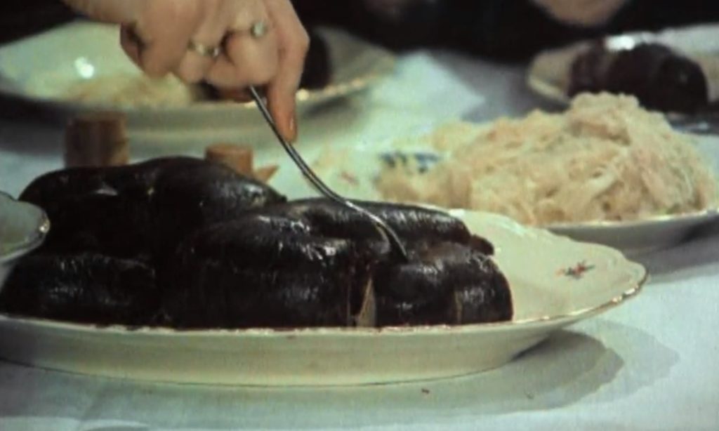 Kadr z filmu "Brunet wieczorową porą". Nabieranie na widelec kawałka kaszanki z talerza. W tle kiszona kapusta na półmisku.