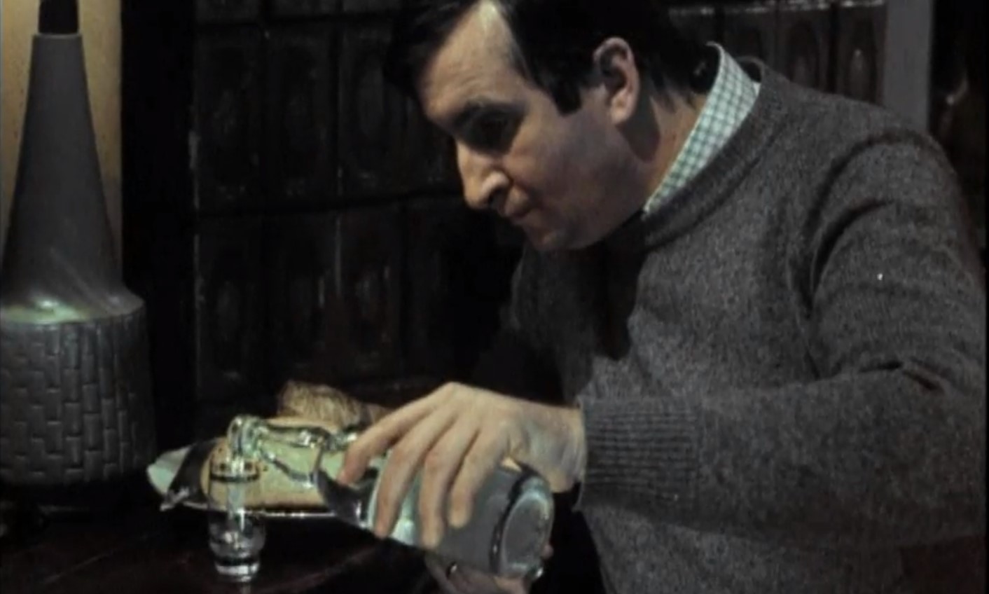 Scena z filmu brunet wieczorową porą. Michał Roman nalewa wódkę do kieliszka.